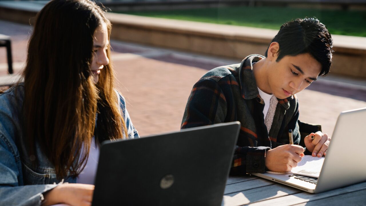 Dwoje studentów pracujących na laptopach przy stoliku na zewnątrz